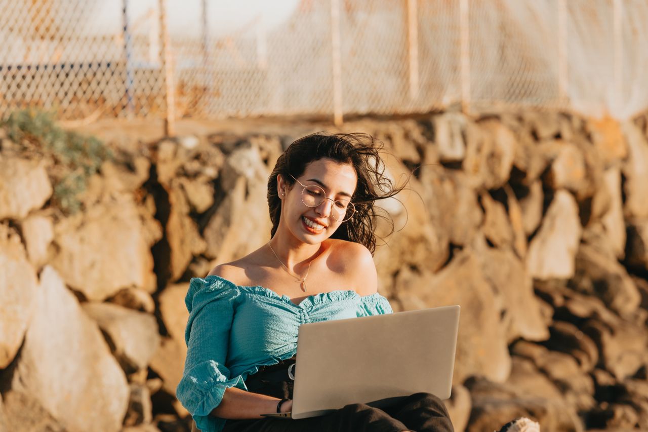The Art of Drawing Readers In: Your attractive post title goes here Woman enjoying remote work with laptop outdoors, smiling on a windy day.